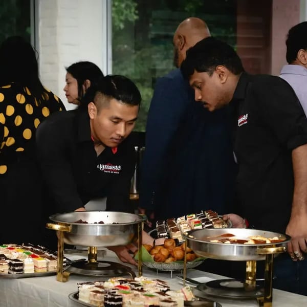 Namaste Taste of India staff serving Indian desserts and pastries from chafing dishes at an event.