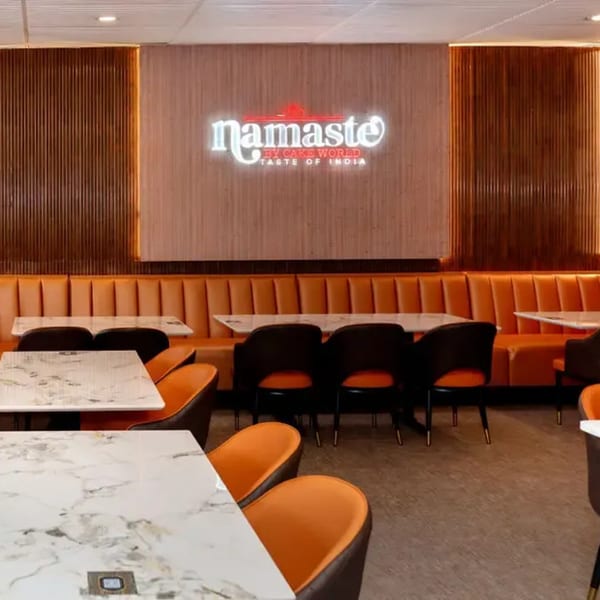 Interior of Namaste Taste of India restaurant with orange booth seating, marble tables, and a neon sign.