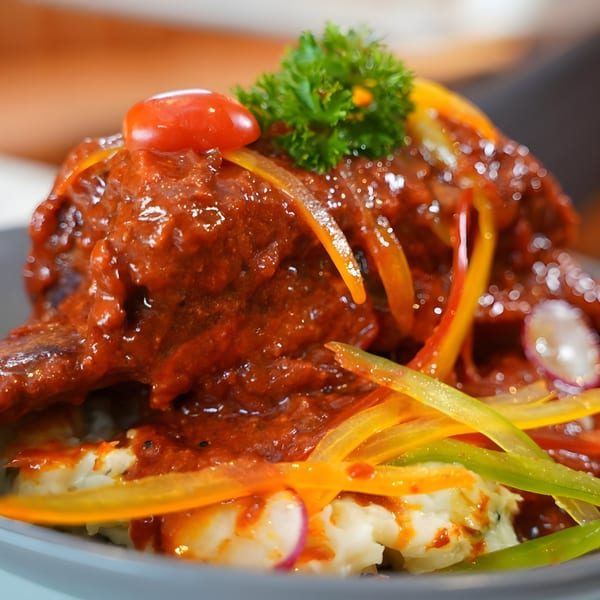 Indian dish with red sauce, mashed potatoes, bell peppers, cherry tomato, and parsley.