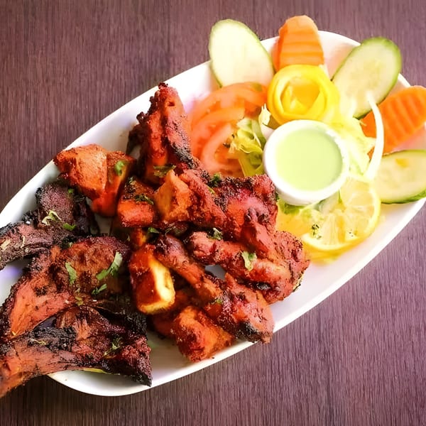 Indian chicken tikka and tandoori chicken with salad, lemon, and green sauce on a white plate.