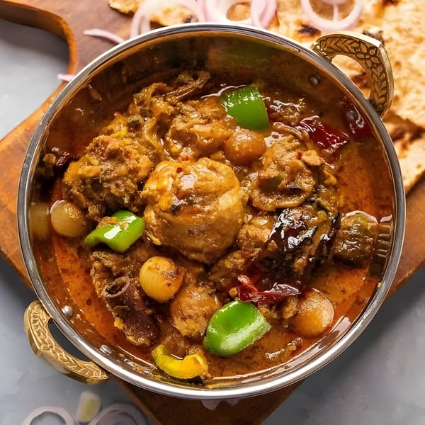 Indian chicken curry with bell peppers and onions in a metal bowl, with naan bread.