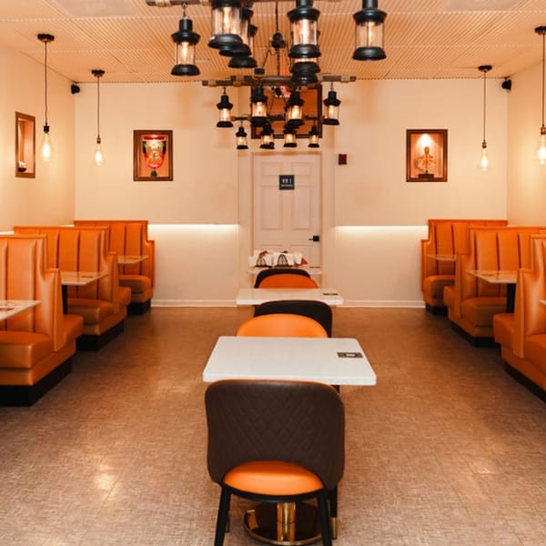 Interior of Namaste Taste of India restaurant with orange booths, tables, and a large chandelier.