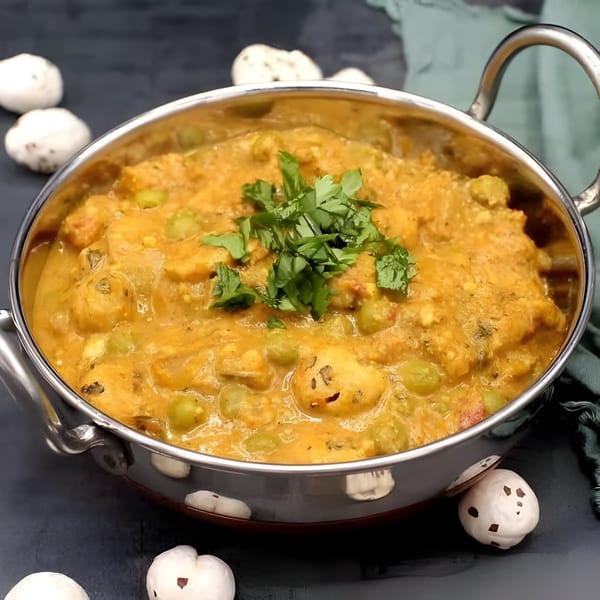 A stainless steel bowl of creamy Indian curry with peas and paneer, garnished with fresh cilantro.