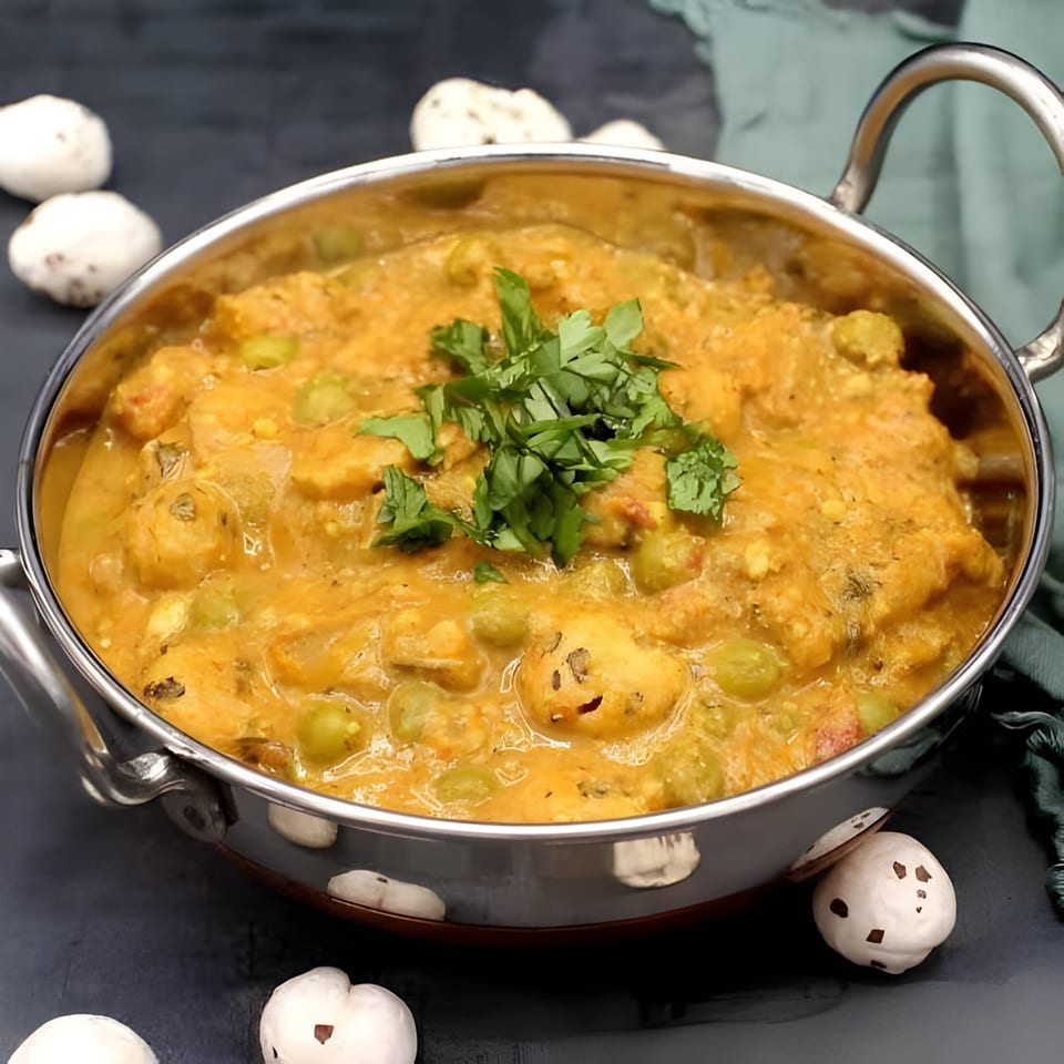 A stainless steel bowl of creamy Indian curry with peas and paneer, garnished with fresh cilantro.