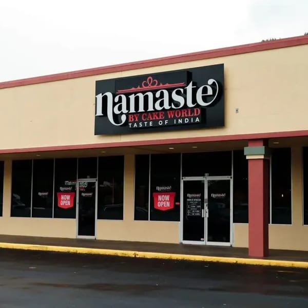 Exterior of Namaste Taste of India restaurant with a large sign and "NOW OPEN" banners on windows.